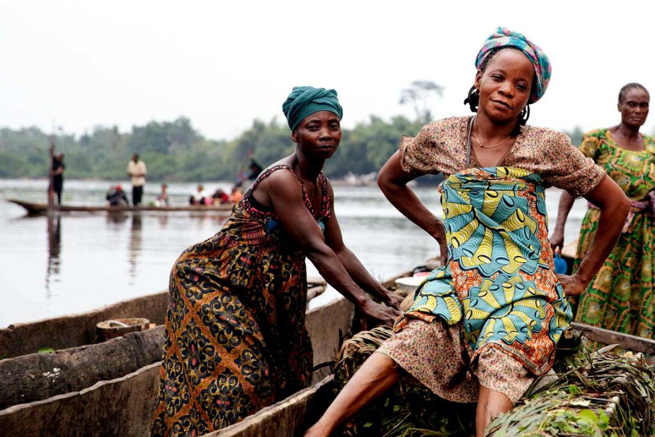 three women are seen standing on boats at the forefront of this photo. In the far back are more boats with people in them.