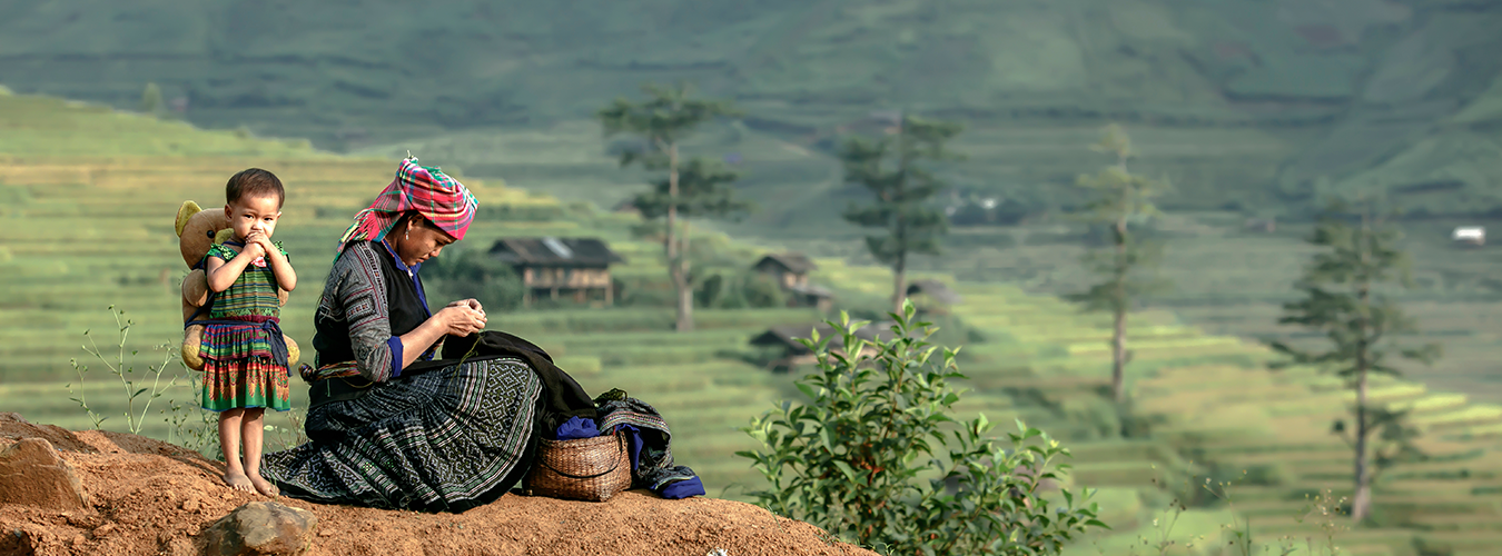 Two indigenous Vietnamese people, mother and child, are sewing morning clothes in front of the hut.