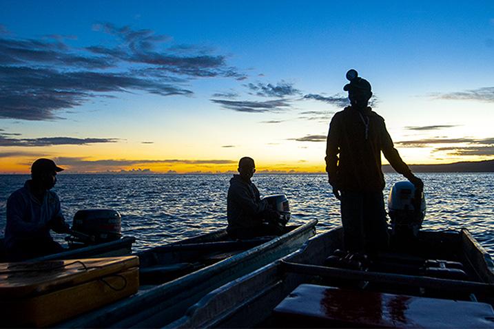 Three men in two artisanal boats in the sunrise