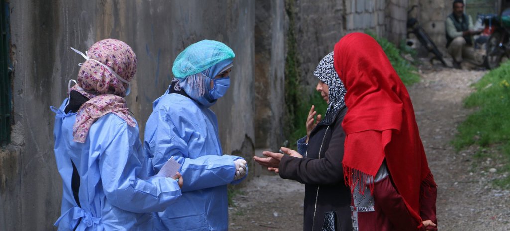 two women in face masks and protective gear taking the temperature of two other women wearing hijabs