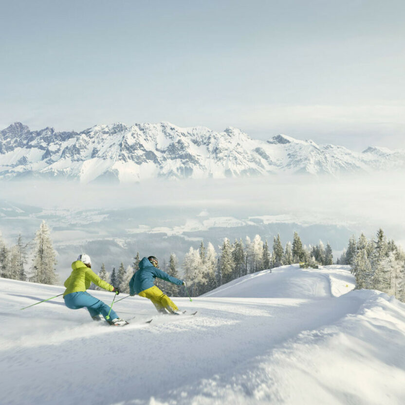 Zwei Skifahrer rasen eine Piste in Schladming-Dachstein runter.