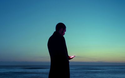 Man looking at phone by the water at night