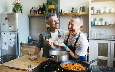 Mid adult cheerful gay couple talking and having fun while cooking in a kitchen