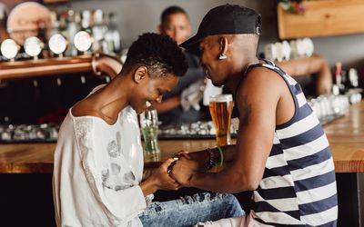  Beautiful smiling and affectionate couple holding hands whilst seated at bar drinking beer