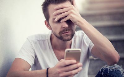 A sad white man with beard looks at phone