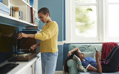 Woman playing music on turntable while partner is using mobile phone on sofa at home