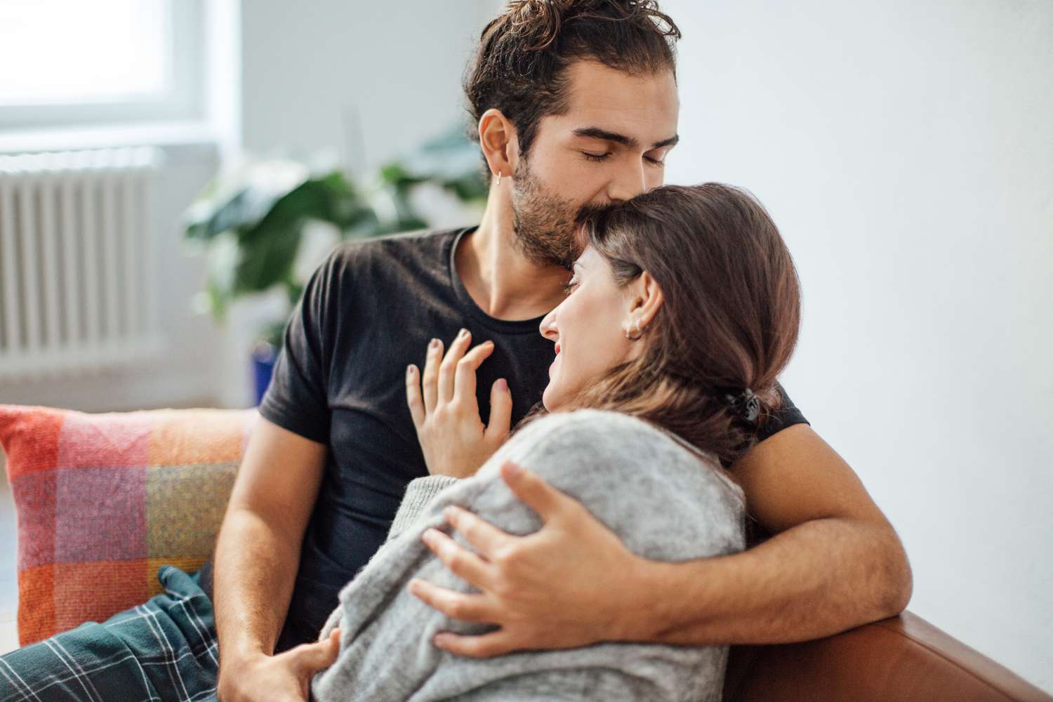 Young man embracing girlfriend while kissing on her forehead in living room at home