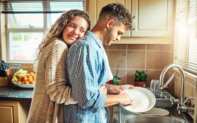 young woman embracing her boyfriend from behind while he does the dishes