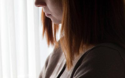 Woman standing near bedroom window, arms crossed