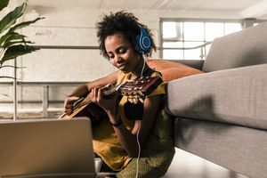 Young woman at home with headphones and laptop playing guitar