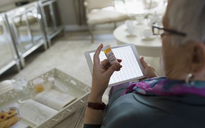 Senior woman reading pill bottle and using tablet