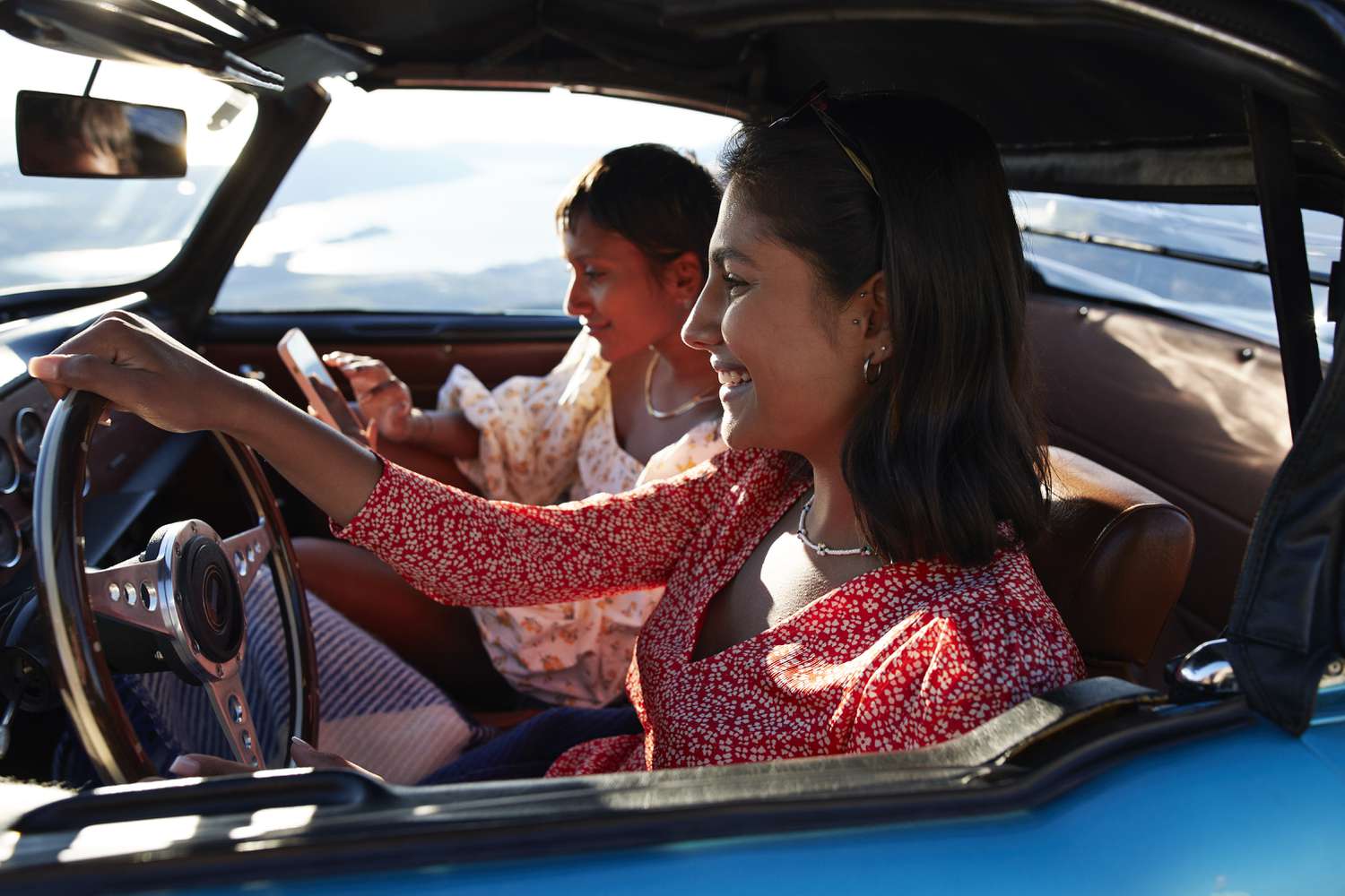 Smiling woman driving car by female friend using smart phone during road trip on vacation