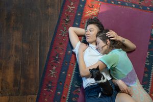 A lesbian couple lying on a rug on the floor and embracing each other affectionately.