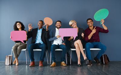 Studio portrait of a group of businesspeople holding speech bubbles while sitting in a row against a grey background