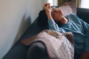 girl sitting on the sofa at home with her hand on her forehead