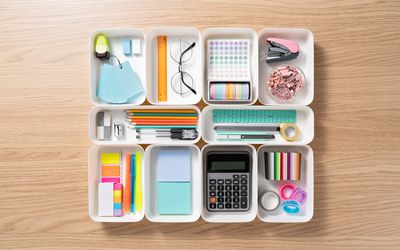 Neatly Organized Stationery in White Trays on Beige Colored Wood Desk Directly Above View.