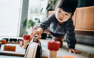 Cute little Asian girl playing with wooden toy train in the living room at home