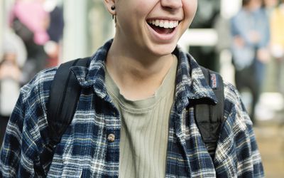 young adult standing in front of a college with their backpack while laughing and smiling