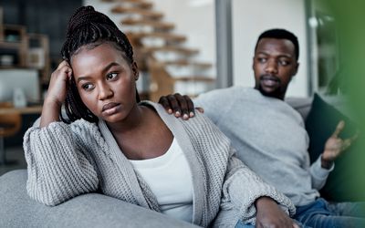 Young man reaching out to his wife after having an argument on the sofa at home