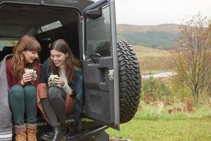 two women sitting in the back of an open car drinking coffee in the autumn