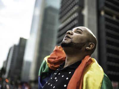 Young queer man holding rainbow flag during pride parade