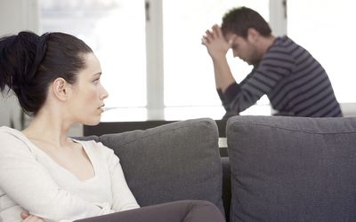 Young woman sitting on sofa, looking at distressed man at table