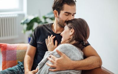 Young man embracing girlfriend while kissing on her forehead in living room at home