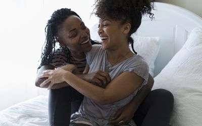 Lesbian couple relaxing on bed, hugging, laughing