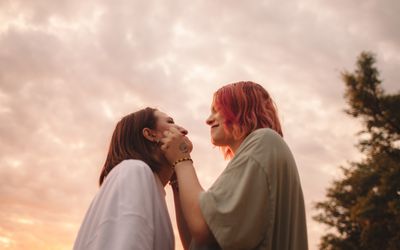 Happy young woman touching her girlfriends cheeks at sunset