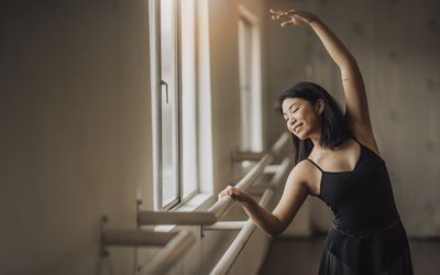 an asian chinese female ballet dancer practising in ballet studio near window waist up