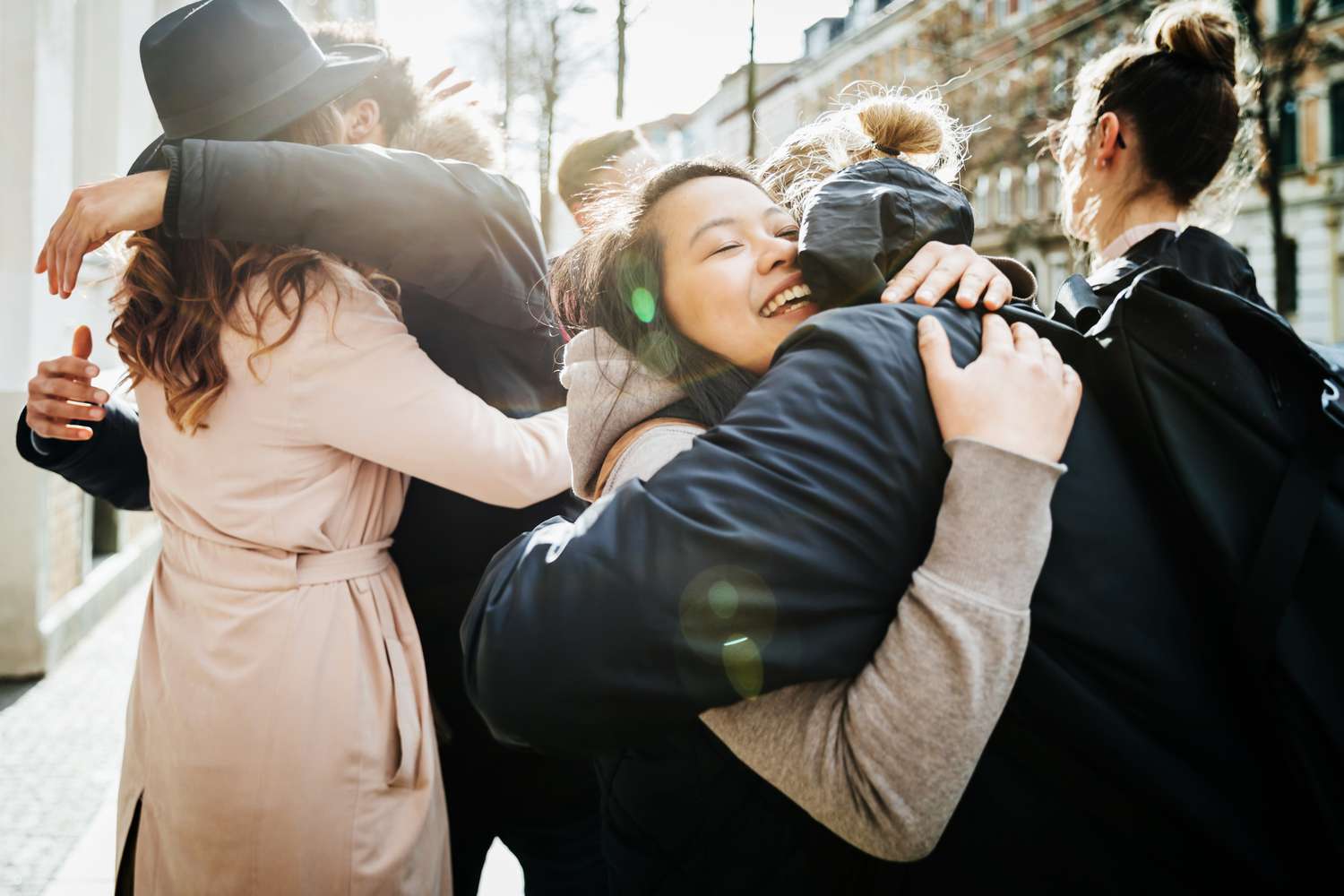 A group of friends meeting up and hugging and smiling with each other before going to a cafÃ© together.