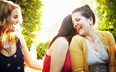 Group of girlfriends sitting on bench outdoors at sunset laughing