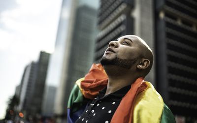 Young queer man holding rainbow flag during pride parade