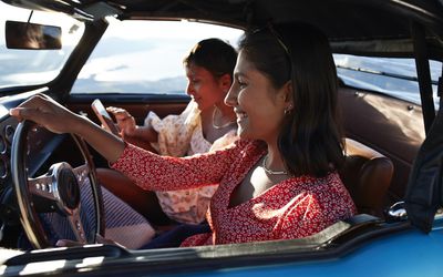 Smiling woman driving car by female friend using smart phone during road trip on vacation