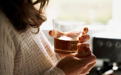 glass cup between hands woman with a glass of whiskey in her hands in front of a window