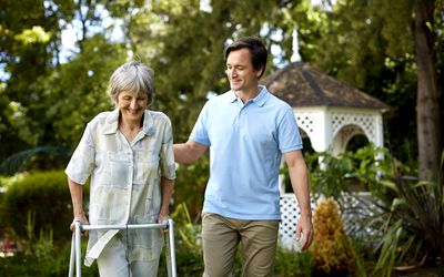 Male caretaker assisting senior woman in using walker at park