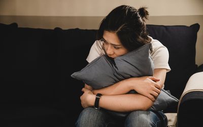 Depressed asian woman sitting on sofa holding a cushion