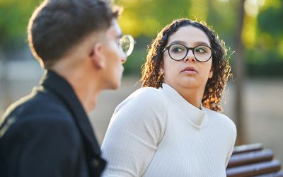 Young woman keeping distance and rejecting a man while having a date together outdoors in a park.