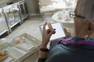 Senior woman reading pill bottle and using tablet