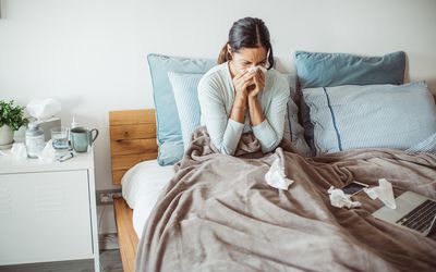 Woman with a cold blowing her nose in bed