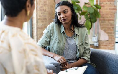 The young adult woman focuses completely on the advice being given by the unrecognizable female therapist.