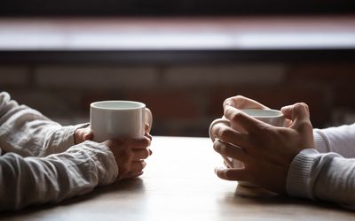 Close up woman and man sitting in cafe, holding warm cups of coffee on table