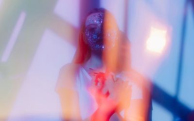 Stylish film looking portrait of pretty teenage girl with beads on her face and colorful flares around her posing with closed eyes