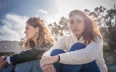 Two sullen young friends sitting on breezy beach