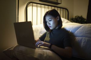 Woman working on her laptop in her bedroom at night