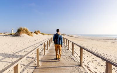 Man walking on boardwalk among sand dunes by the ocean