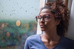 Sad african american girl looking out of the window on rainy weather