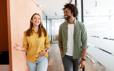 Couple of business people discussing tasks walking in the office hall. Two diverse colleagues have small talk during break. Friendly atmosphere in team