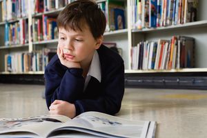 Young boy reading large book in school library.