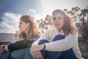 Two sullen young friends sitting on breezy beach